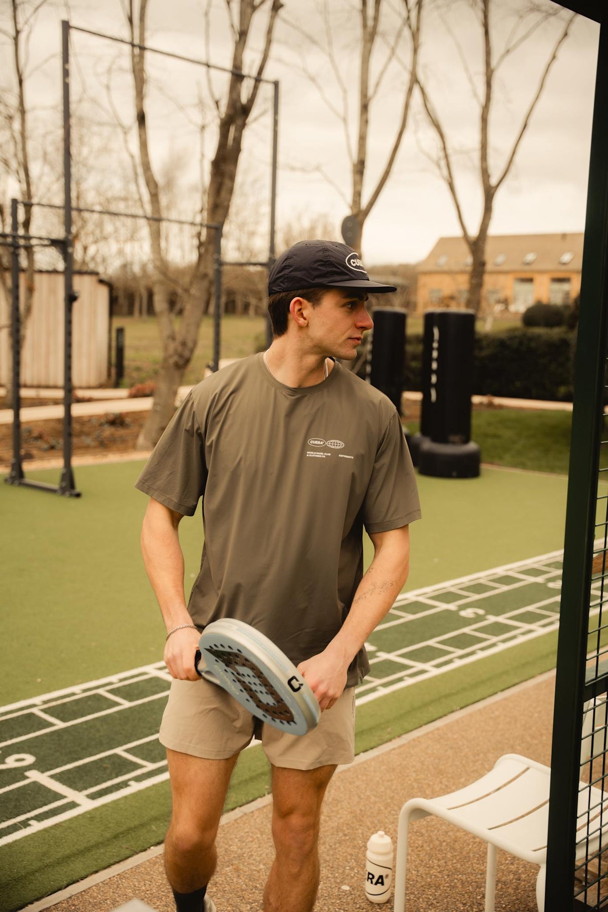 Model wearing Cuera Oncourt Airy Logo T-Shirt in Army, lifestyle action shot on the padel court