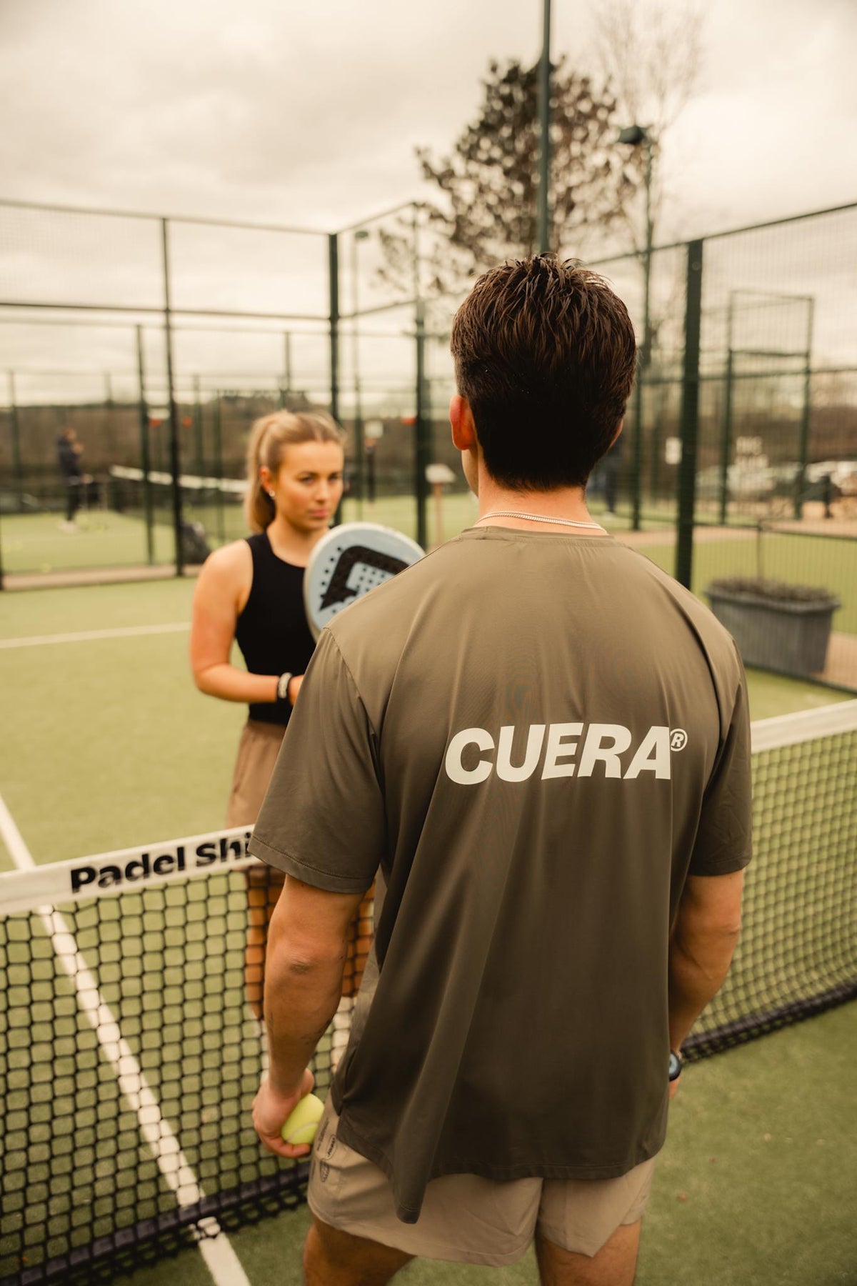 Model wearing Cuera Oncourt Airy Logo T-Shirt in Army, lifestyle action shot on the padel court
